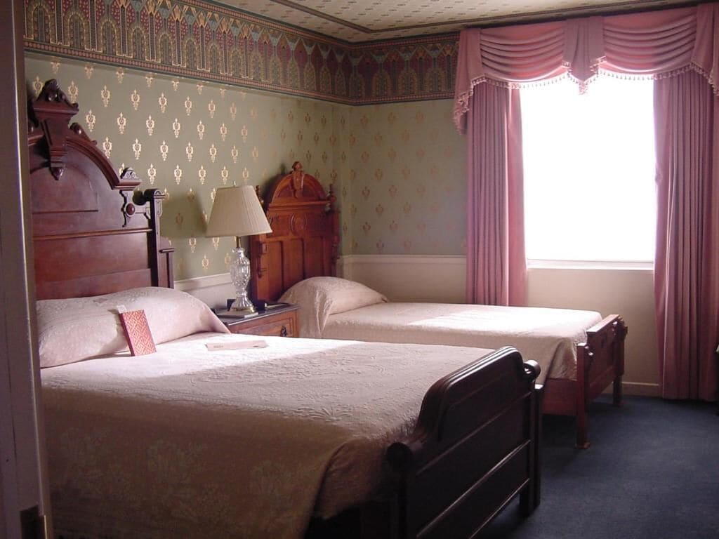 Une chambre avec deux lits, une table de chevet avec une lampe et une fenêtre avec des rideaux.