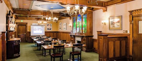 A hotel dining area with wooden paneling, chandeliers, and a projection screen.