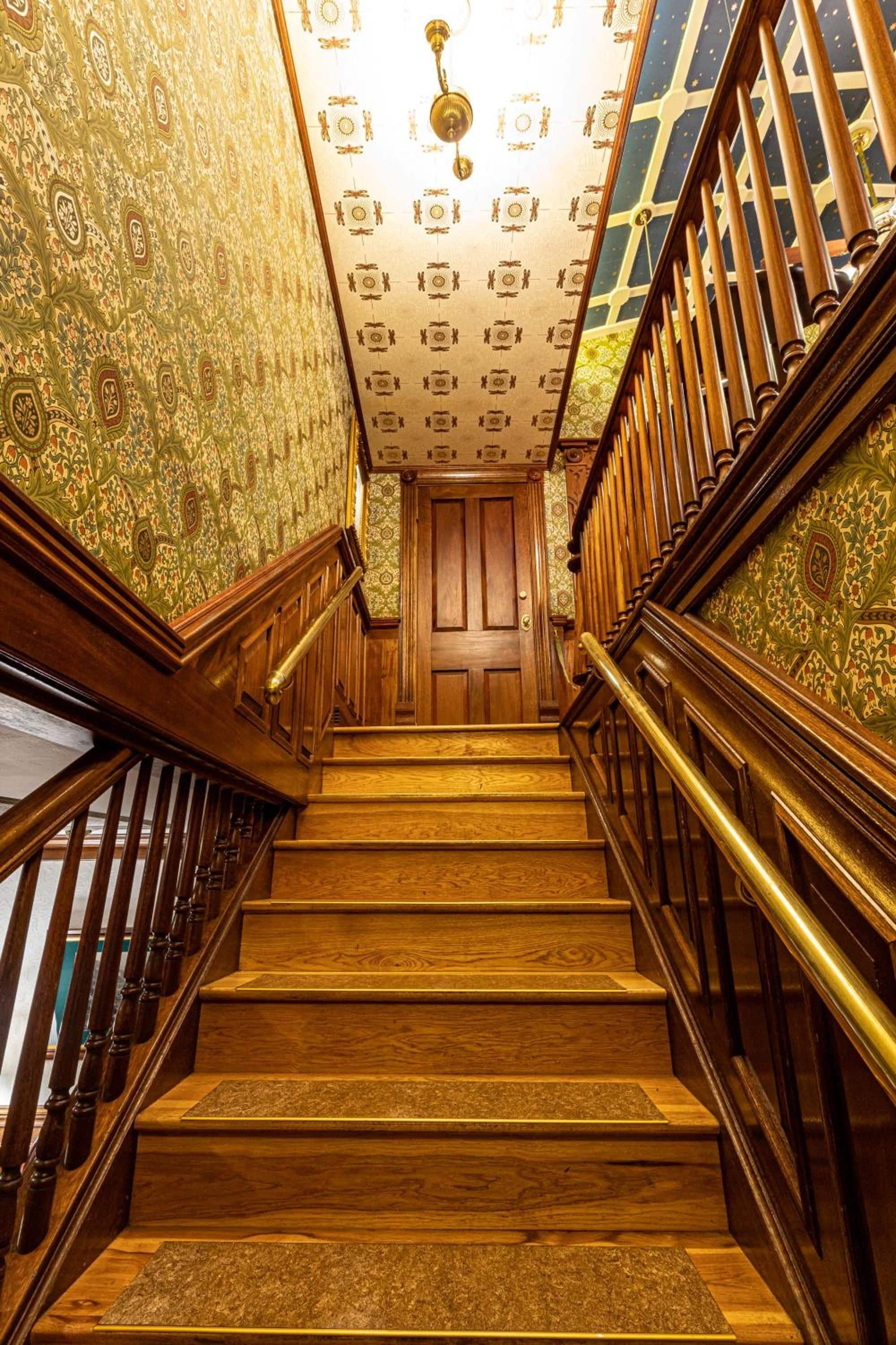 A wooden staircase with ornate railings and patterned wallpaper.