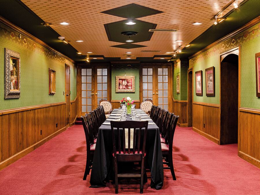 Un salón de conferencias con una mesa larga dispuesta para una reunión, rodeada de sillas, paredes verdes y paneles de madera.