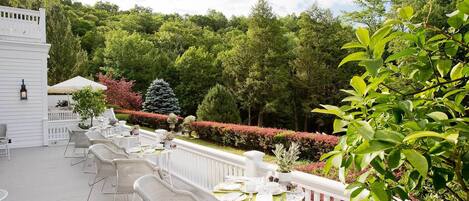Un patio cubierto al aire libre con mobiliario de mimbre blanco y una valla blanca.