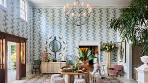 A room with patterned wallpaper, a chandelier, a round table with stools, a fireplace, and a large plant. - Mayflower Inn & Spa, Auberge Collection (Washington)