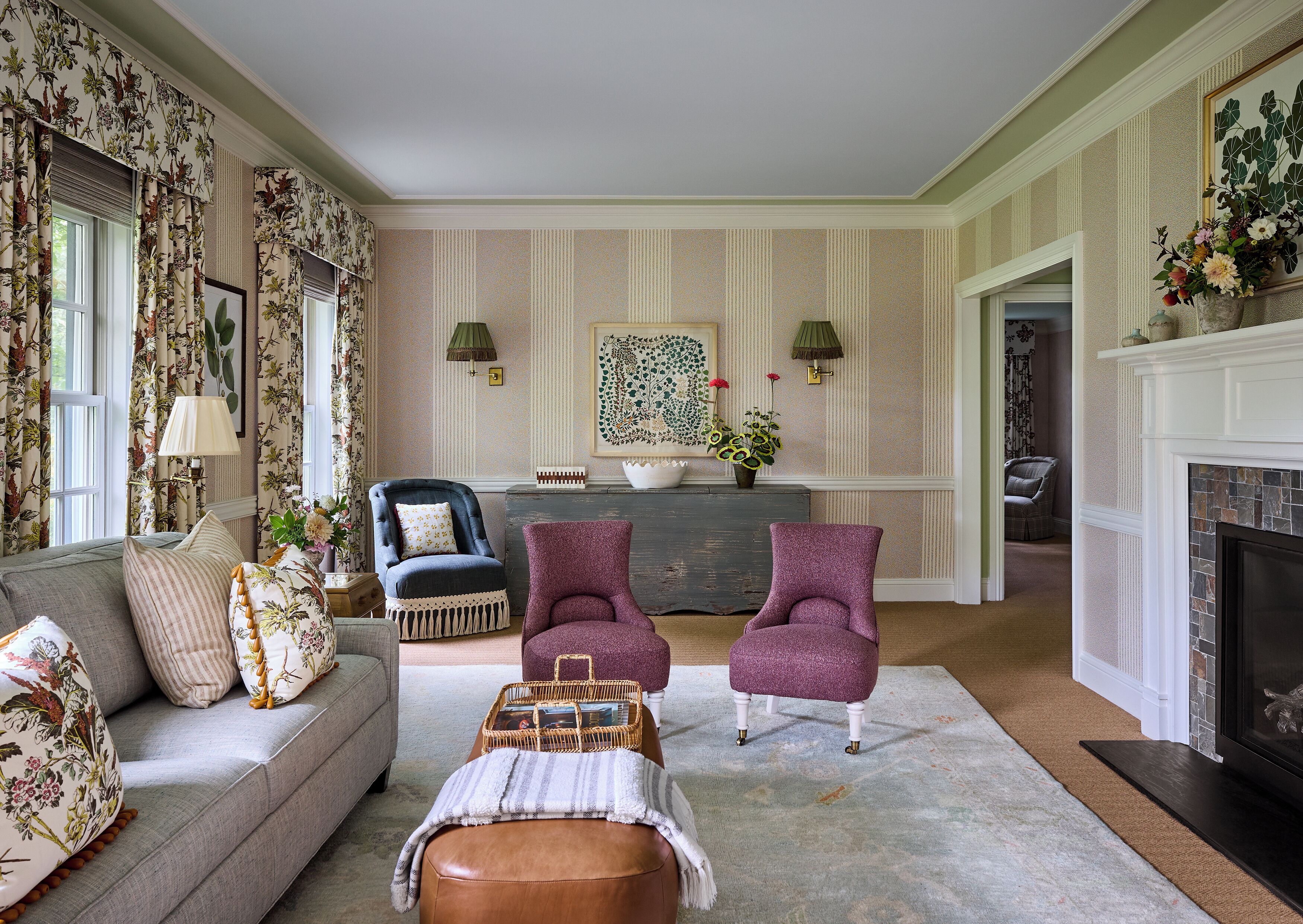 A living room with a sofa, two armchairs, a coffee table, a fireplace, and a decorative wall with a painting.