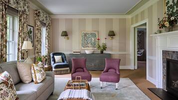 A living room with a sofa, two armchairs, a coffee table, a fireplace, and a decorative wall with a painting.