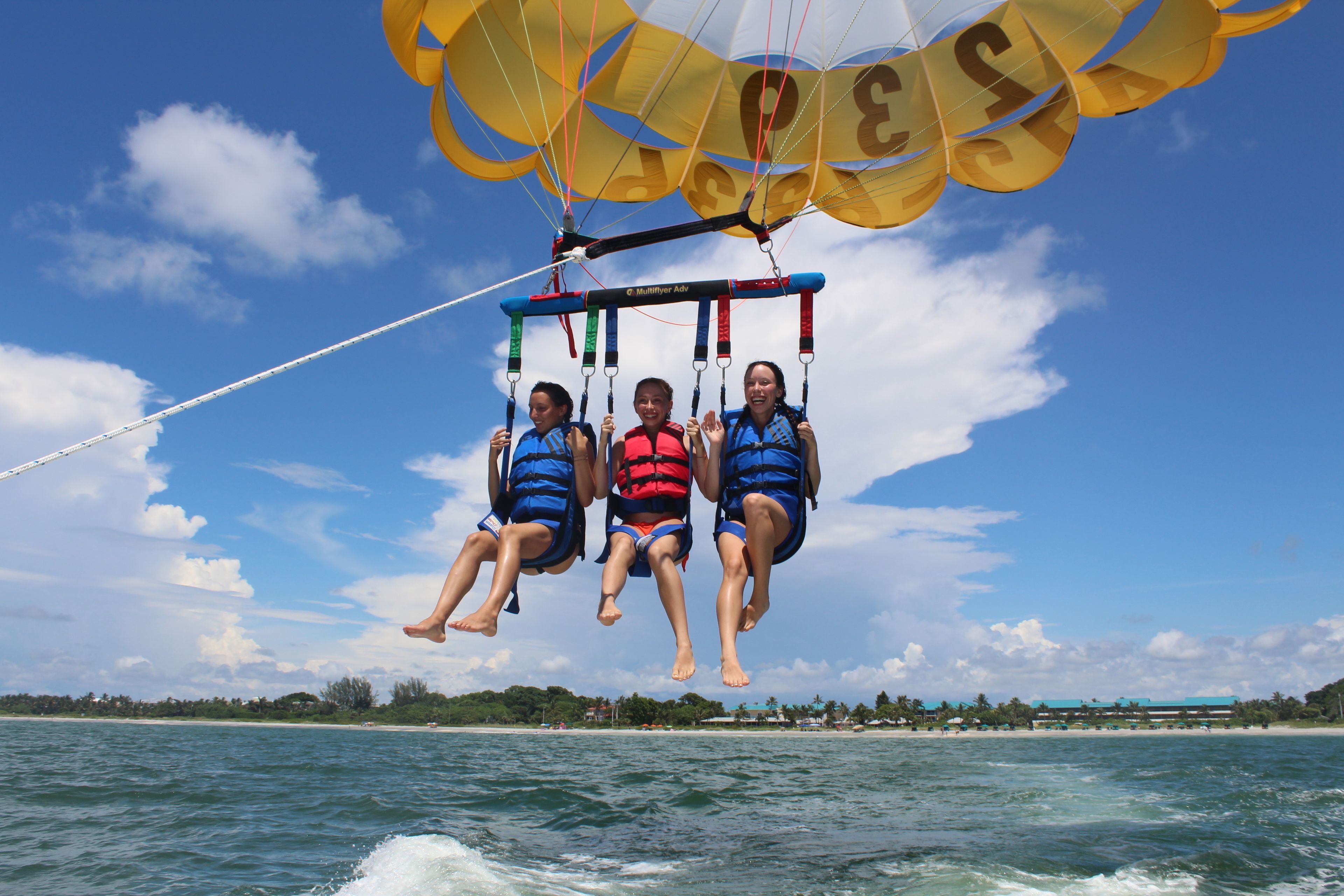 Three people parasailing over water with a clear sky and a distant shoreline.