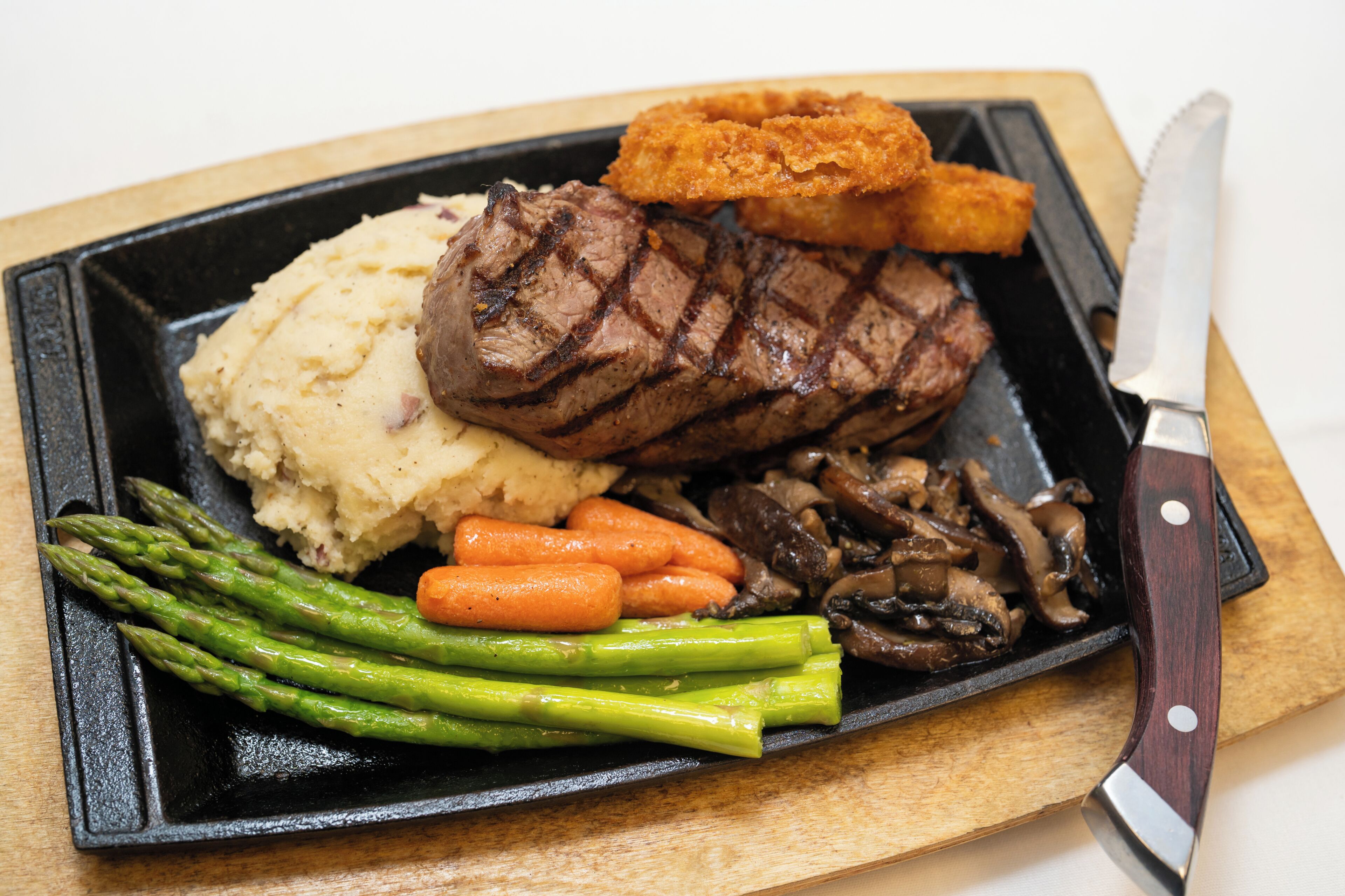 A steak with vegetables and a knife on a cutting board.