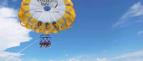 A parasail with 'TWEEN WATER'S INN' branding, over a beach with clear skies.