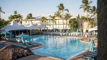 A swimming pool with lounge chairs and umbrellas, surrounded by palm trees and hotel buildings.