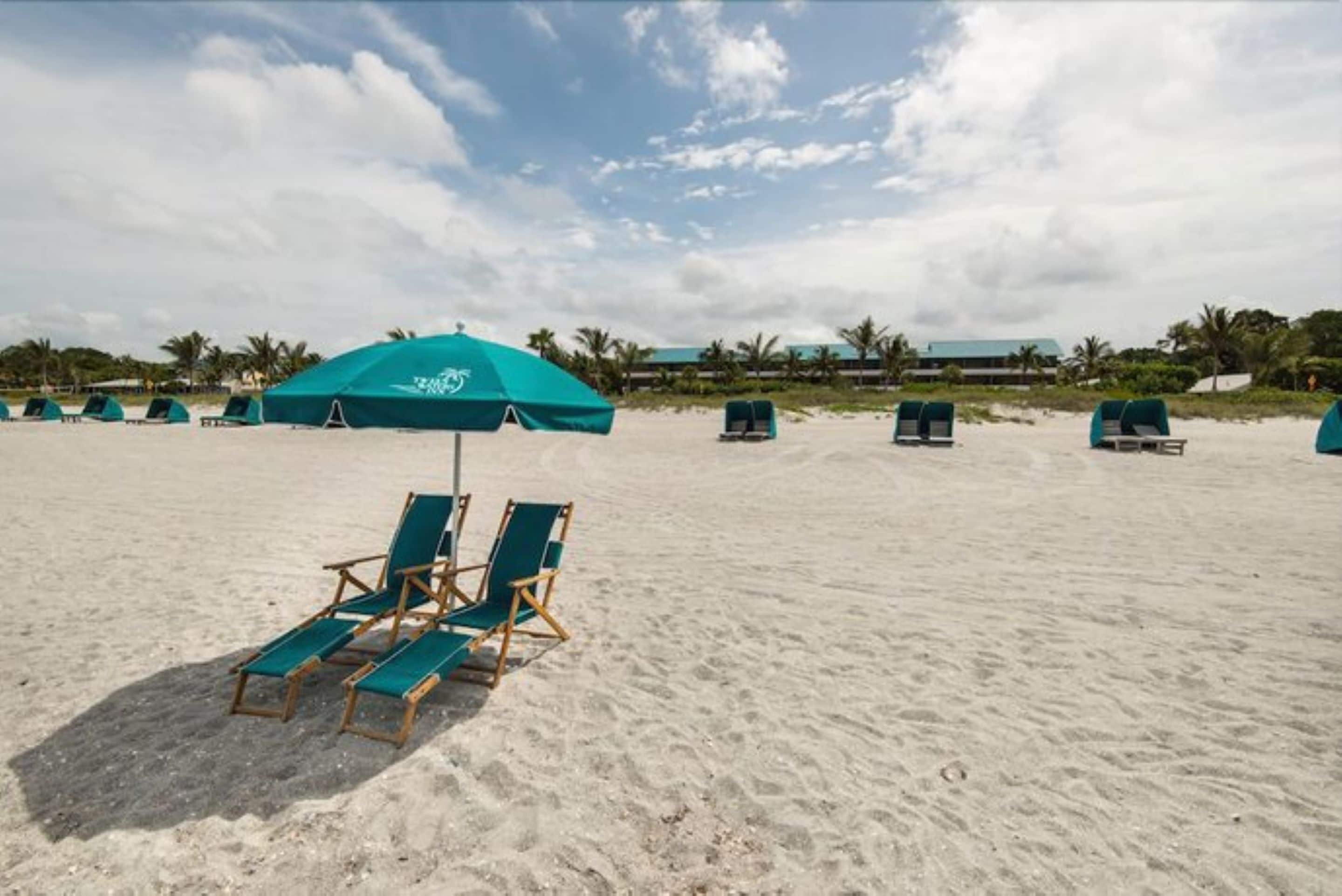 A beach with several turquoise umbrellas and lounge chairs.