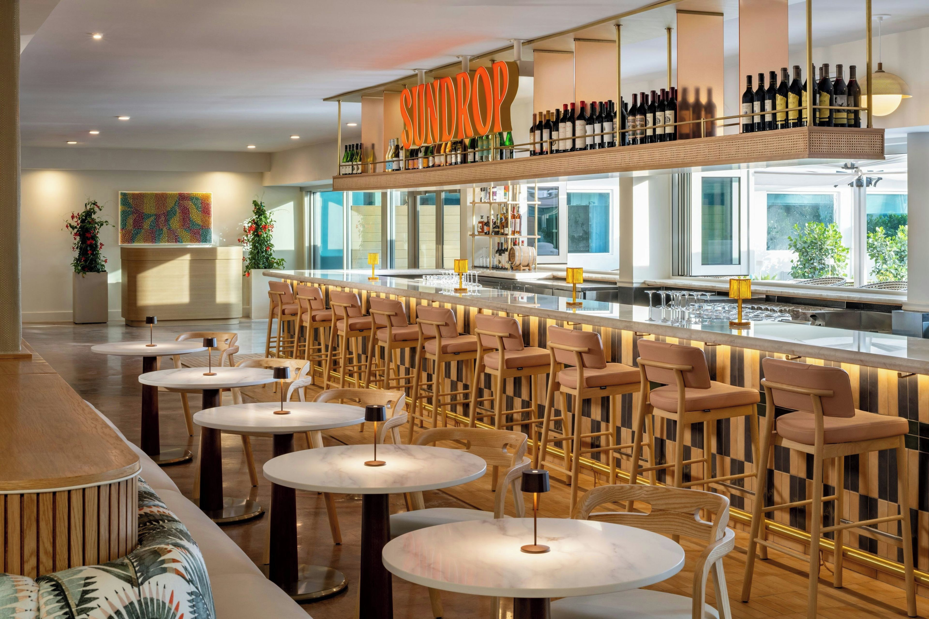 A bar area with multiple seating options, including round tables and bar stools, and a variety of bottles displayed on shelves.