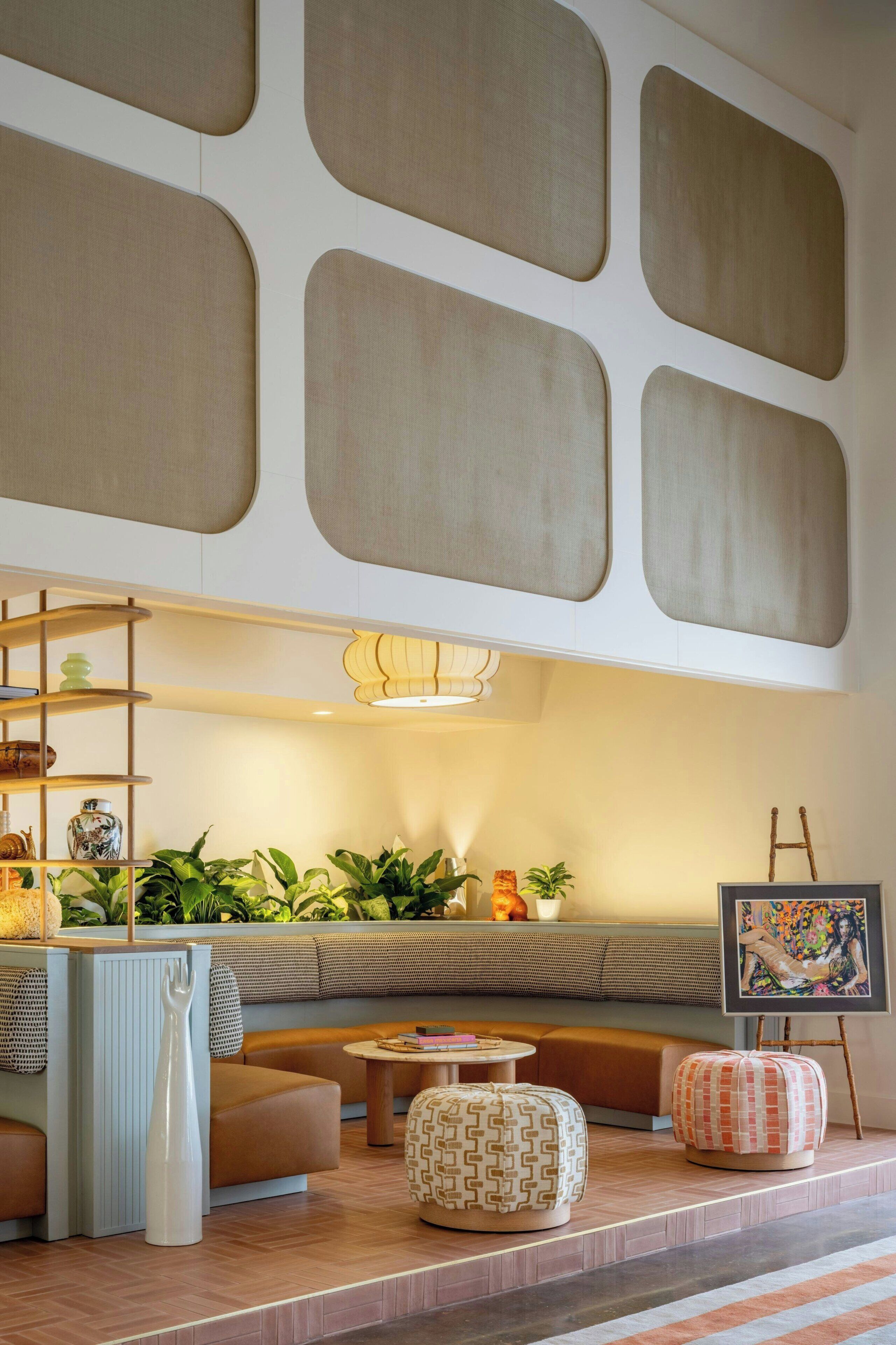 A modern lounge area with a sofa, ottomans, a ladder, and a painting on easel.