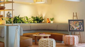 A modern lounge area with a sofa, ottomans, a ladder, and a painting on easel.
