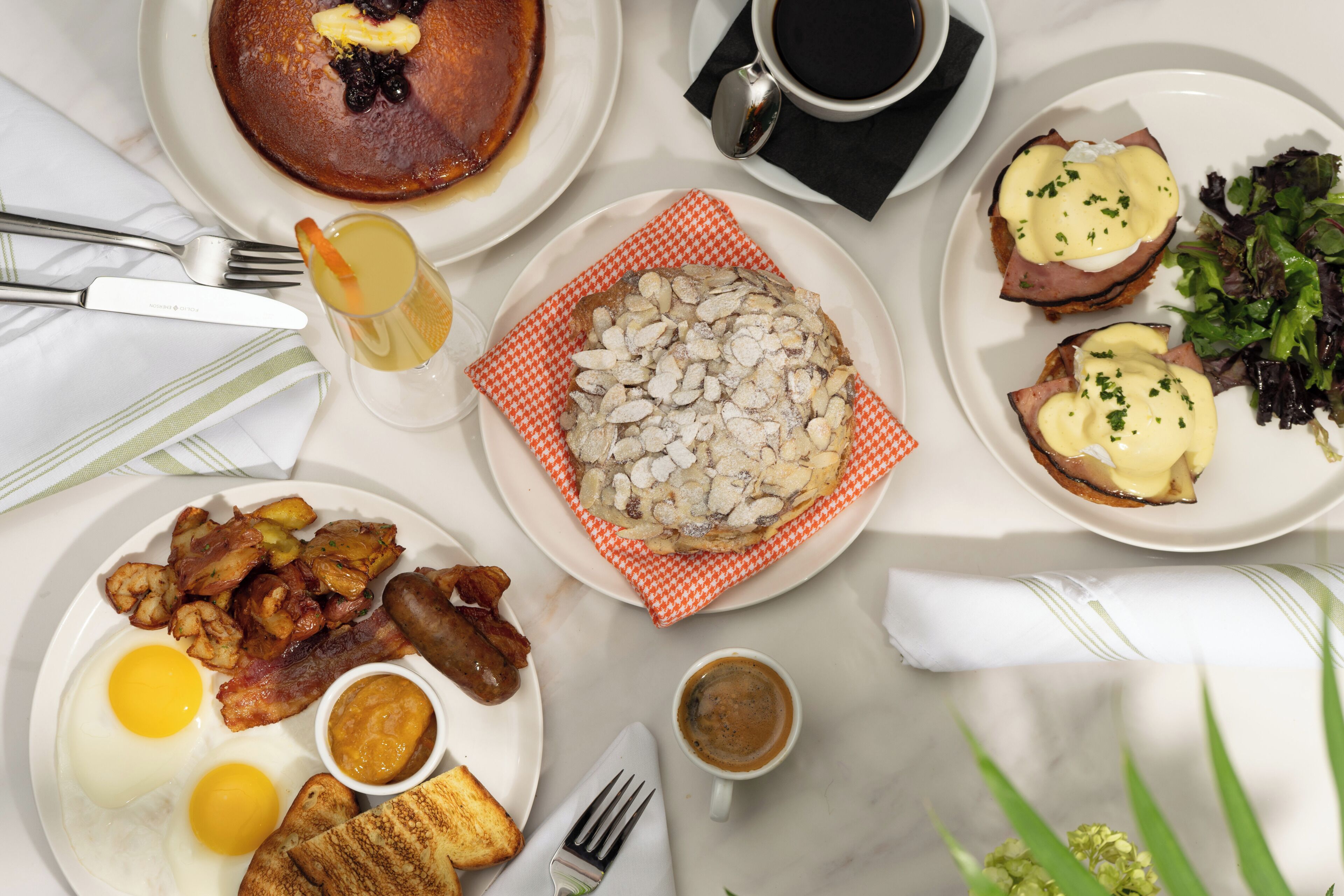 Una mesa de desayuno con diferentes platos, como panqueques, huevos, tocino, tostadas y café.