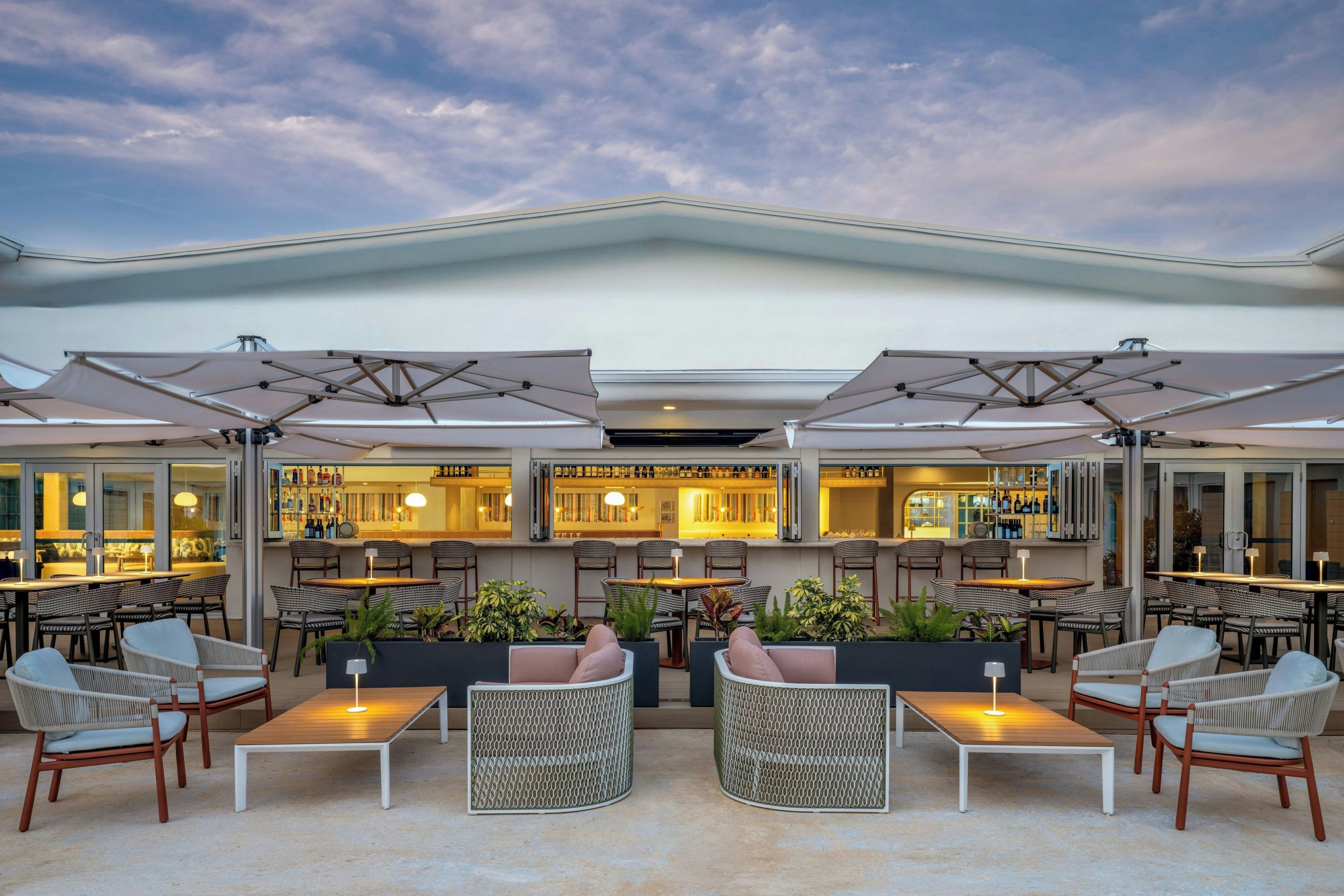 An outdoor seating area with tables and chairs, a bar with bottles, and a view of the sky.