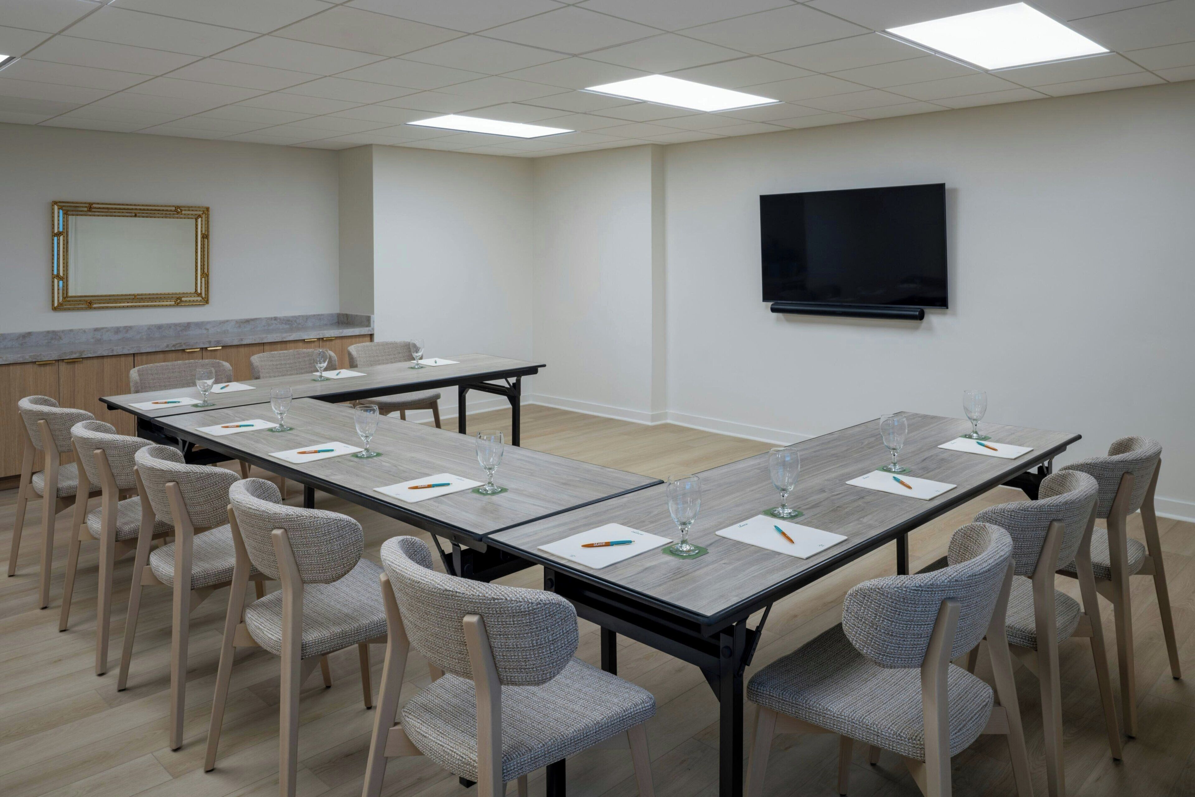 A conference room with a long table, chairs, a TV, and a mirror.