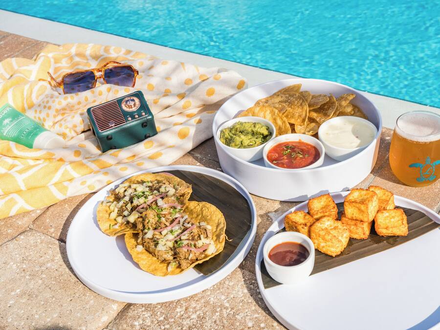 A poolside setting with a table set for a meal including tacos, chips, and beverages.