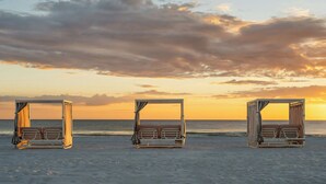 Una playa con tres camas abiertas alineadas paralelamente a la orilla, cada una con dosel y almohadas.