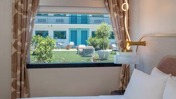A hotel room with a bed, a window with curtains, a view of the outdoor area, and a lamp on the bedside table.