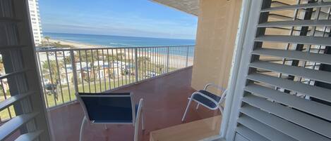 Un balcon avec vue sur la plage et l’océan. On y trouve deux chaises et une table.