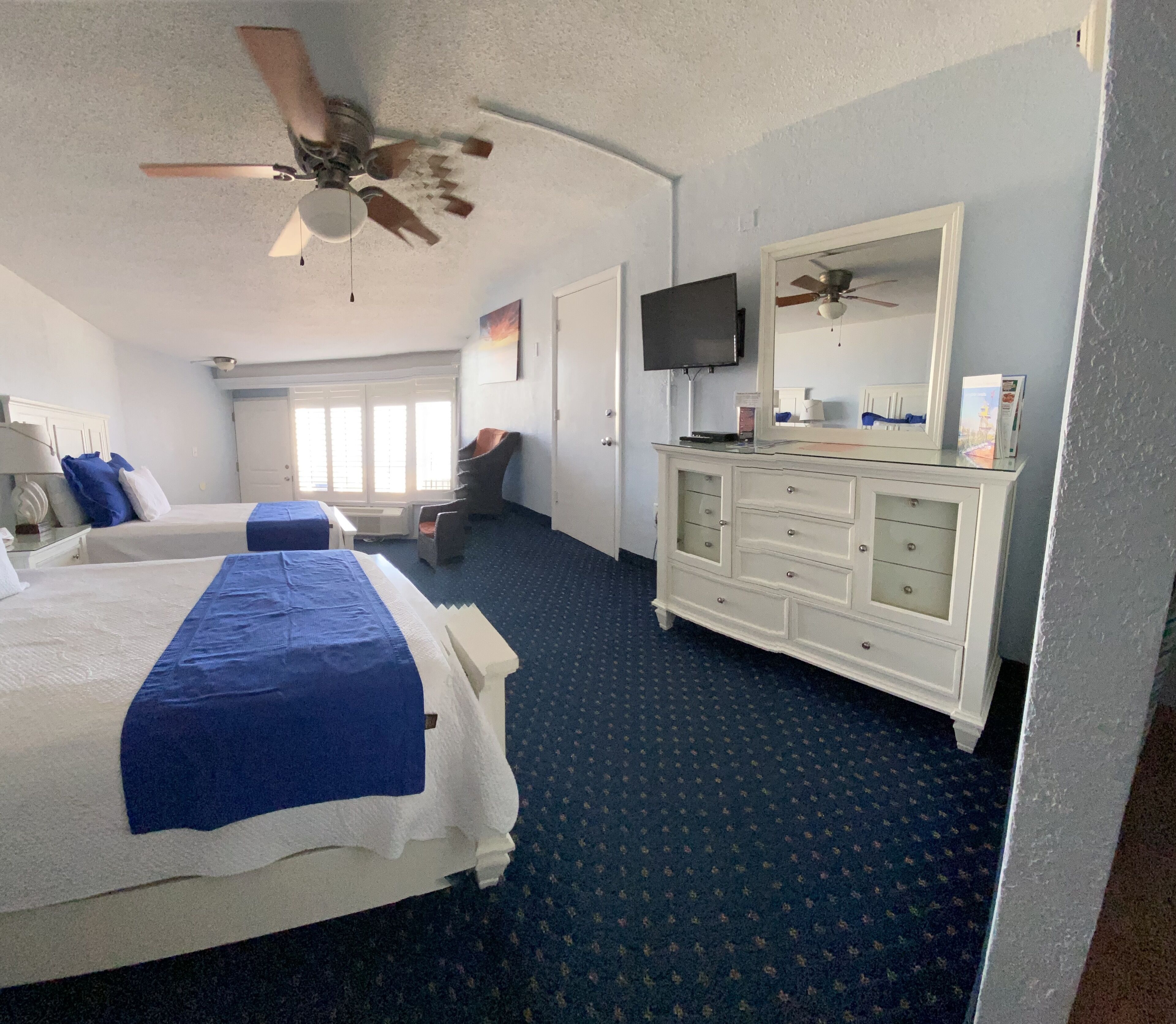 Une chambre d’hôtel avec deux lits, une commode, un téléviseur et un ventilateur de plafond.