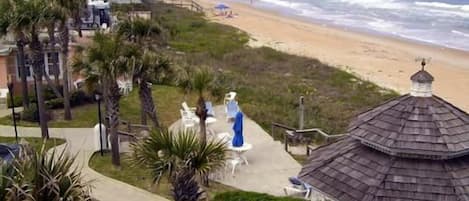 Vista da praia com um gazebô, palmeiras e um caminho que leva à praia.