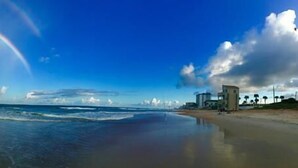 Una playa con olas, un arcoíris y un edificio a lo lejos.