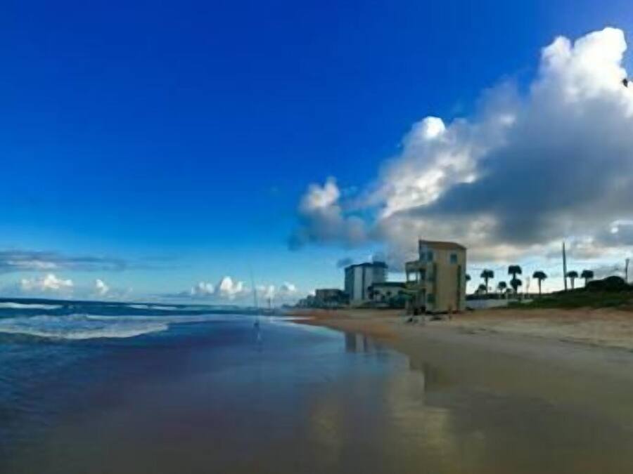 A beach with waves, a rainbow, and a building in the distance.