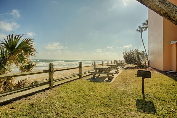 Vista de la playa con una valla de madera, mesas de picnic y un buzón.