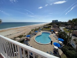 A pool area with lounge chairs and umbrellas, overlooking a beach and ocean.