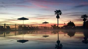 Un área de piscina tranquila con sombrillas y palmeras al atardecer.