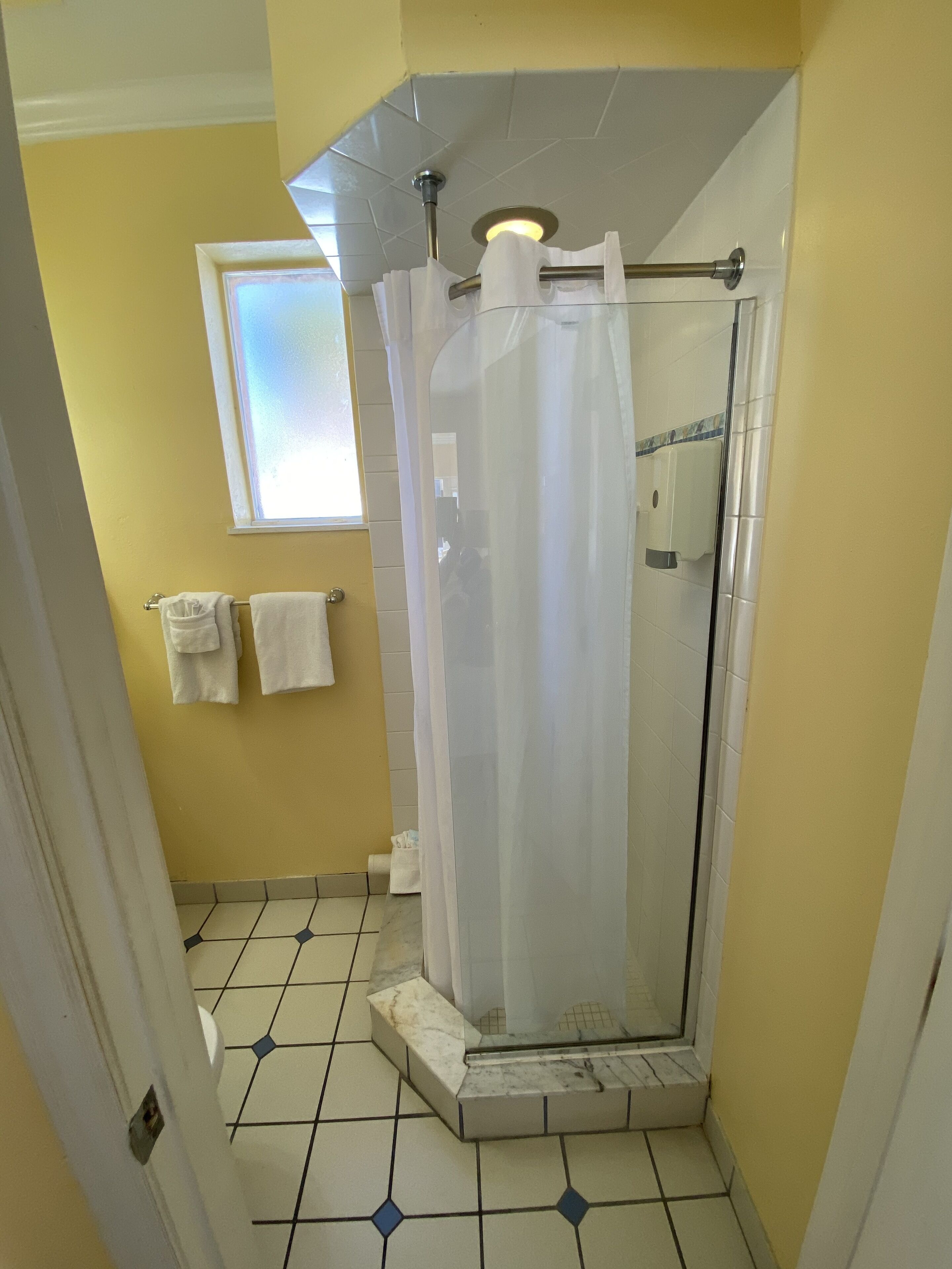 A bathroom with a glass shower enclosure, a window above the sink, and a tiled floor.