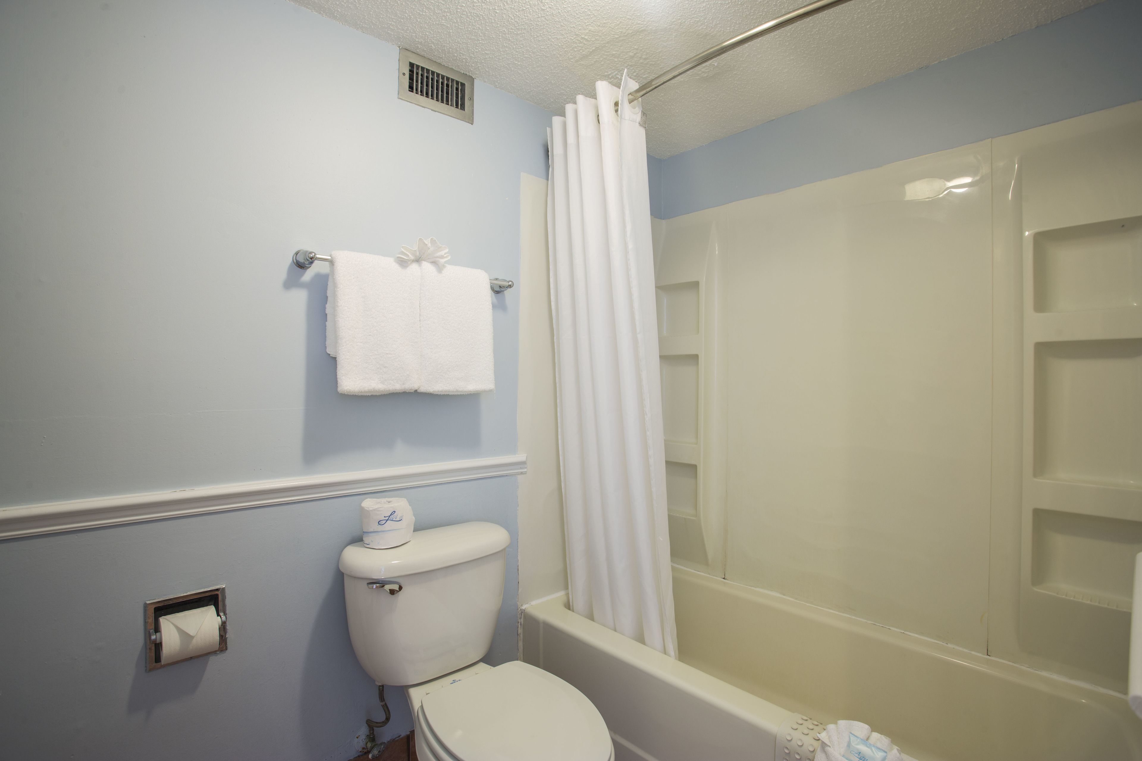 A bathroom with a toilet, a shower with a curtain, and a towel rack.