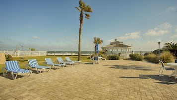 A beachside patio with lounge chairs, a gazebo, and a view of the ocean.