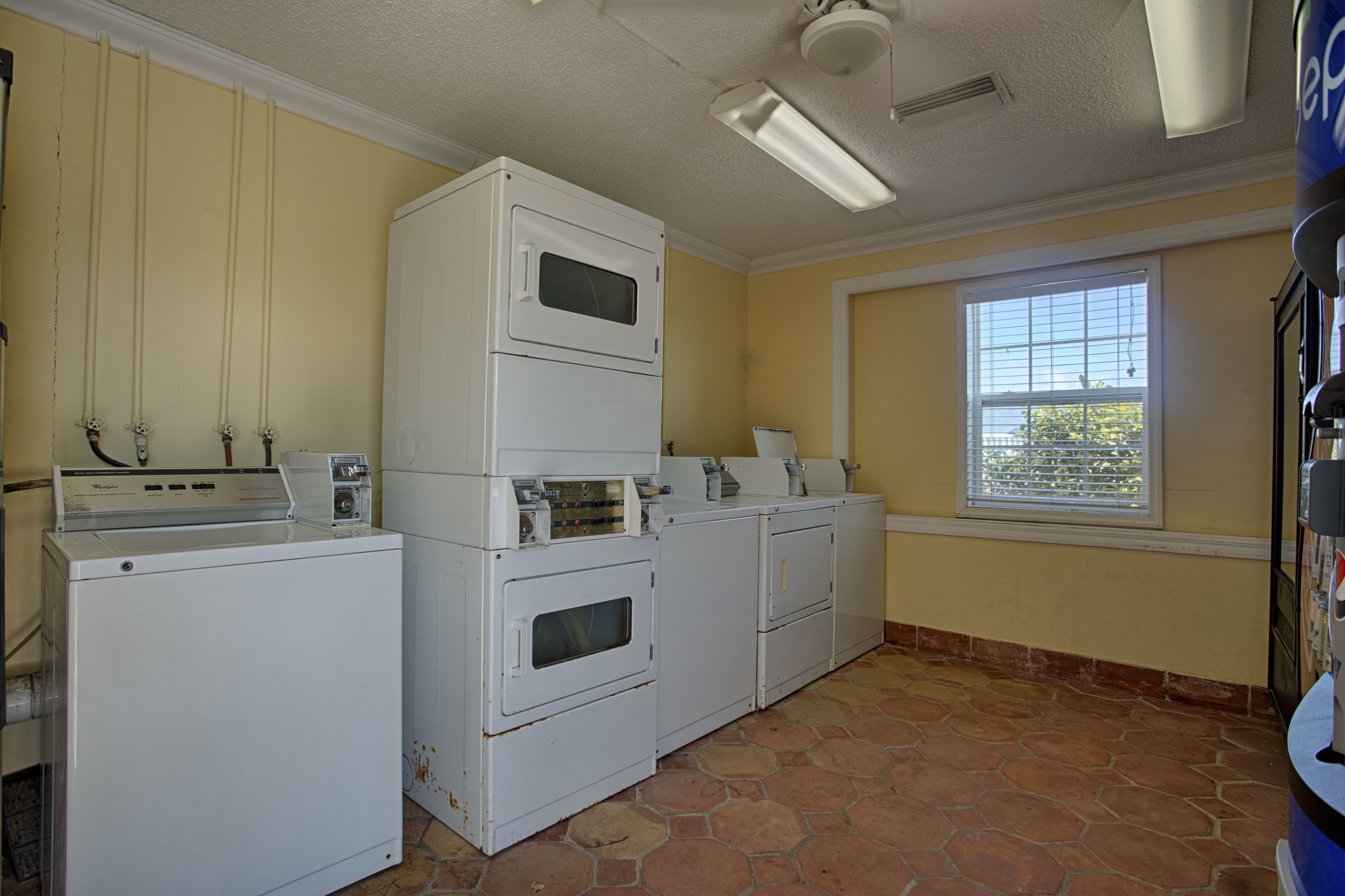 A laundry room with stacked washers and dryers, a window with blinds, and a ceiling fan.