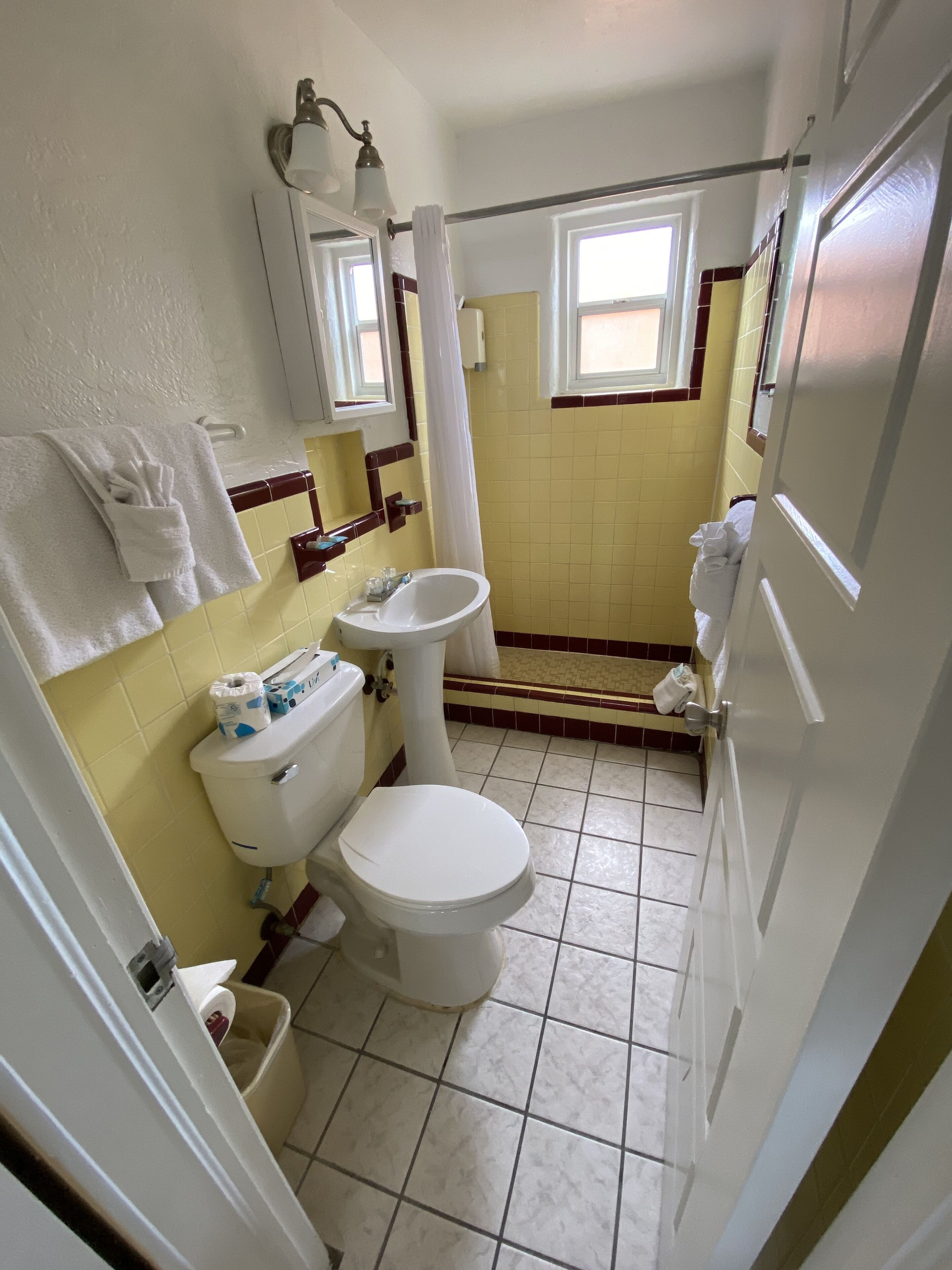 A small bathroom with a toilet, sink, and shower. There are towels hanging on the wall and a window providing natural light.
