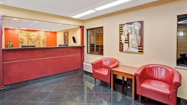 A reception area with a red counter, two red leather chairs, a wooden table, and a wall with a decorative relief and a modern abstract painting. - Economy Inn Jax-OP (Jacksonville)