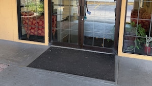 A building entrance with glass doors, a black mat, and potted plants. - Economy Inn Jax-OP (Jacksonville)