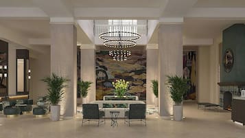 A spacious lobby with a high ceiling, a central chandelier, a dining area with a table and chairs, and a large mural on the back wall.