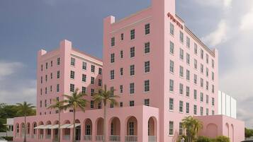 A pink multi-story hotel with a central courtyard, palm trees, and a clear sky.