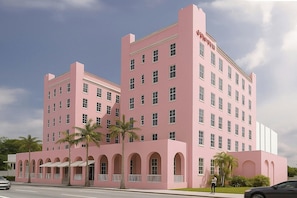 A pink multi-story hotel with a central courtyard, palm trees, and a clear sky. - Gulfstream Hotel (Lake Worth)