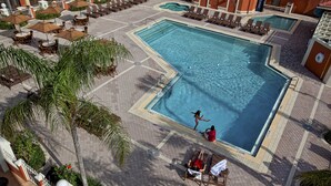A large outdoor swimming pool with sun loungers and umbrellas, surrounded by a tiled walkway and palm trees. - Westgate Towers Resort (Kissimmee)