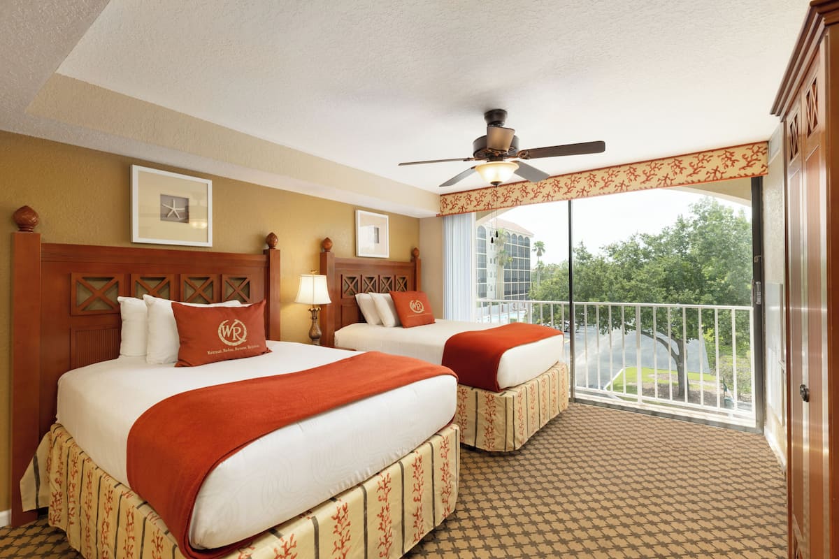 A hotel room with two beds, a balcony with a view, and a ceiling fan.