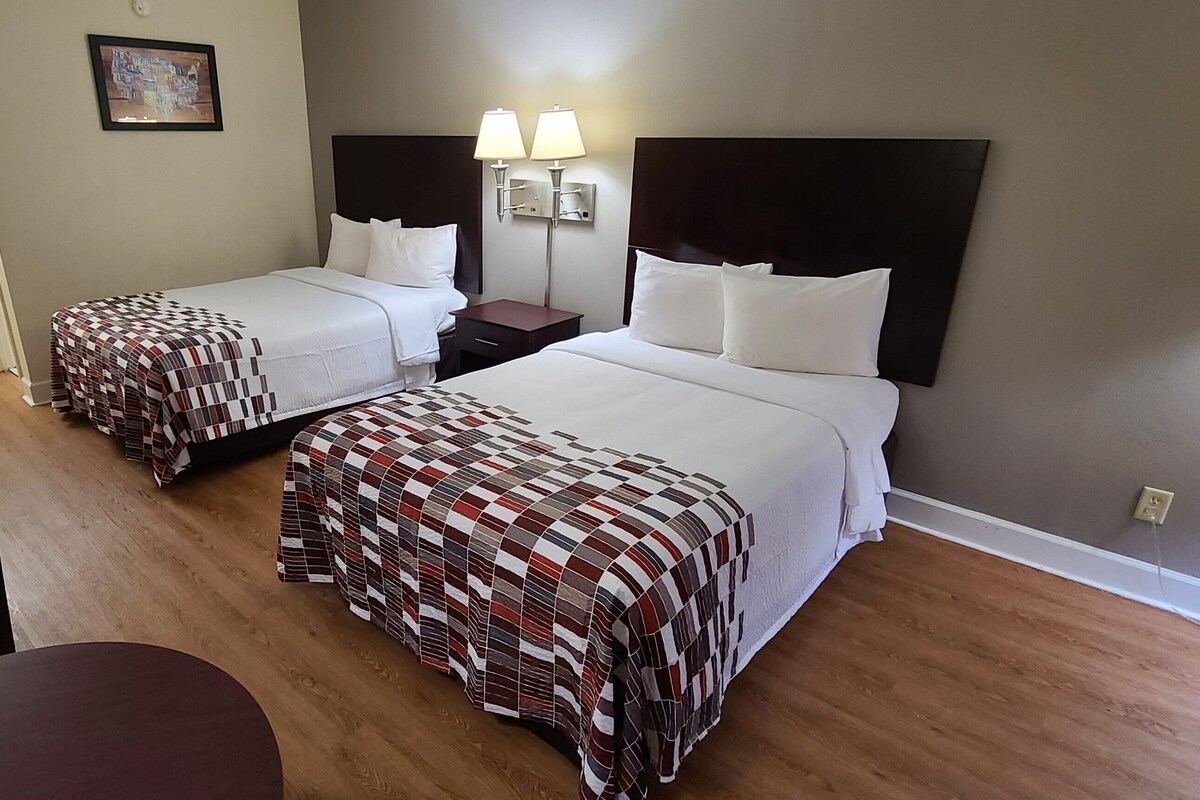 A hotel room with two beds, a desk, a chair, a small table, and a mirror.