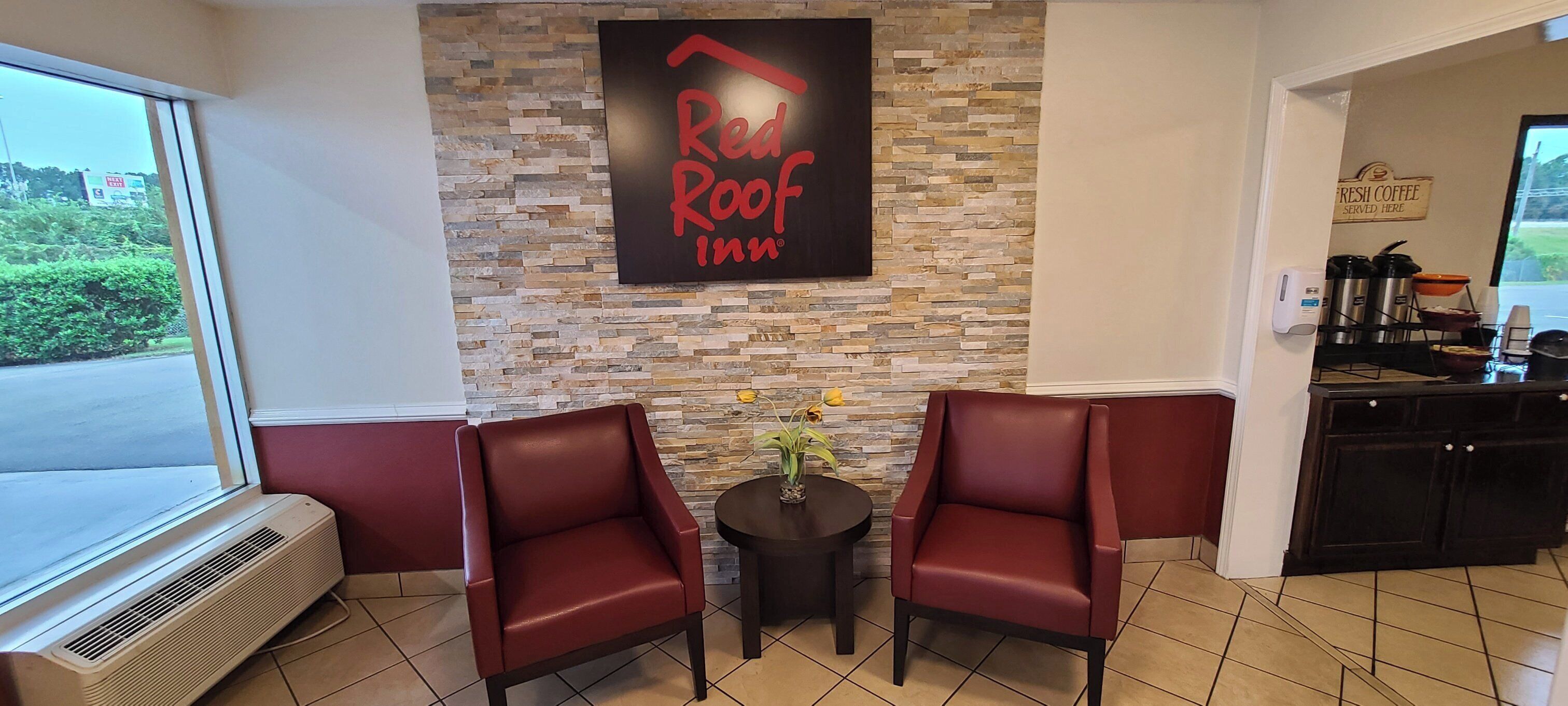 A Red Roof Inn seating area with two red leather chairs, a small table with a vase, and a stone wall.