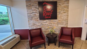 A Red Roof Inn interior with two red chairs, a small table with a vase, and a stone wall. - Red Roof Inn Tifton (Tifton)