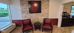 A Red Roof Inn seating area with two red leather chairs, a small table with a vase, and a stone wall. - Red Roof Inn Tifton (Tifton)