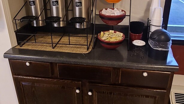 Una encimera de cocina con cafeteras, un bol de fruta y un letrero que dice 'FRESH COFFEE SERVED HERE'.