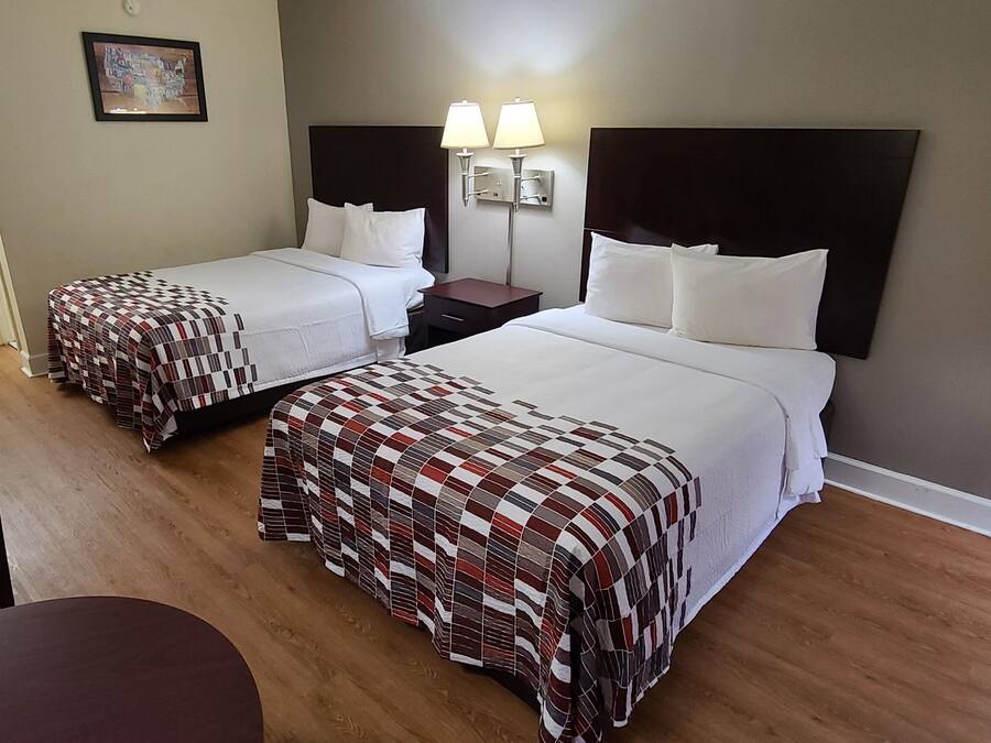 Quarto de hotel com duas camas, uma escrivaninha, uma cadeira, um espelho e uma luminária na parede.