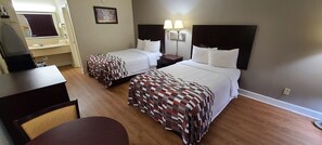 A hotel room with two beds, a desk, a chair, a mirror, and a wall-mounted lamp. - Red Roof Inn Tifton (Tifton)