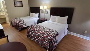 A hotel room with two beds, a nightstand, a lamp, and a painting on the wall. - Red Roof Inn Tifton (Tifton)